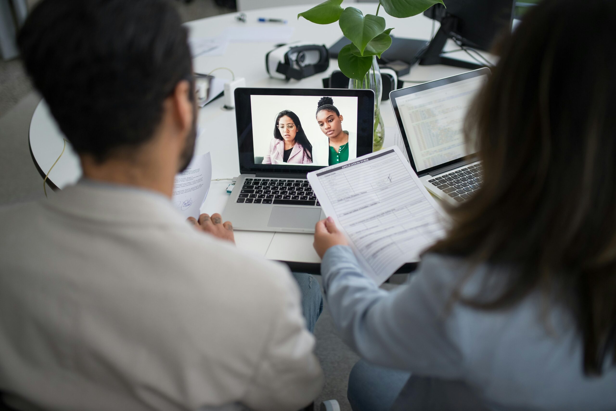 Two professionals conduct a virtual job interview using laptops in a modern office.